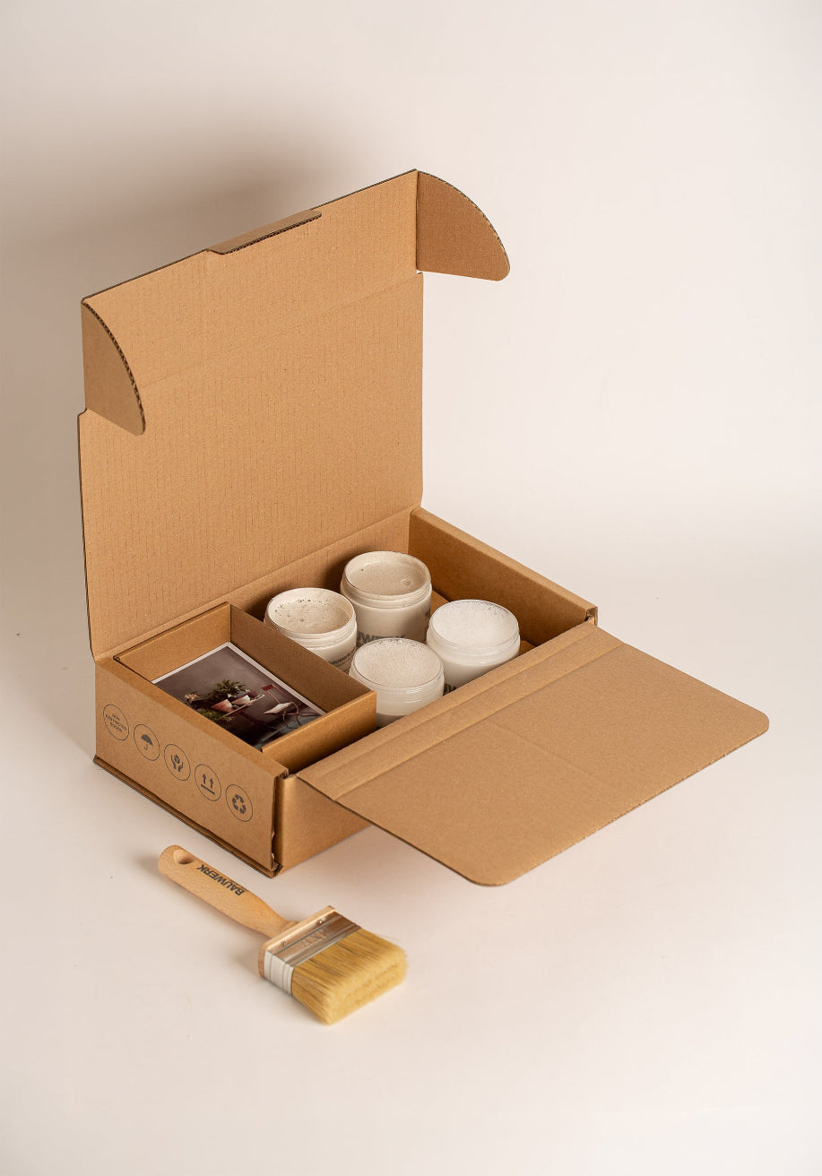 Open Coastal Garden Pot Paint Collection box with four 250ml limewash paint pots in soft chalky white tones, a natural bristle brush and inspiration card. | © Bauwerk Colour